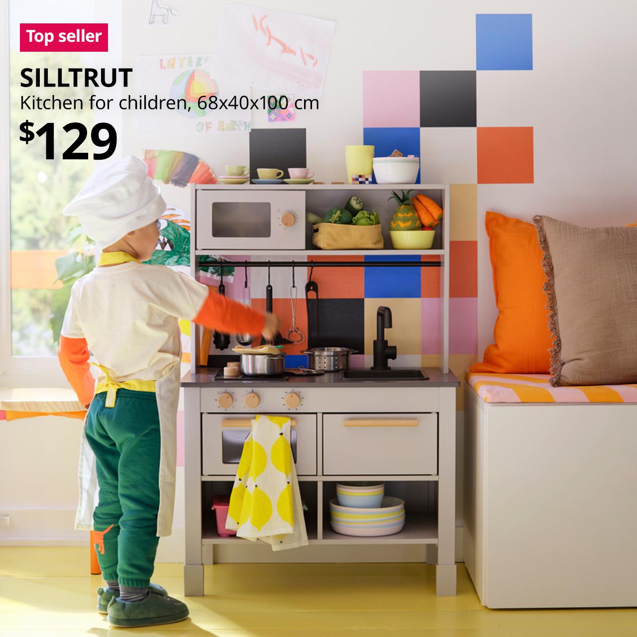 A child playing with a grey SILLTRUT play kitchen for children. Overlaid on the image is a pink/red "Top seller" tag and black text reading "SILLTRUT, Kitchen for children, 68x40x100 cm, $129".
