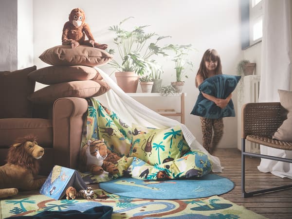 A child playing with DJUNGELSKOG and pillows in the living room.