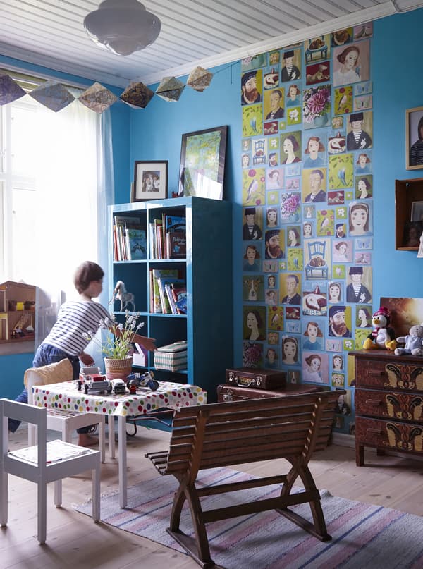 A child plays in his bedroom with natural wood floors and blue walls that match the book shelf.