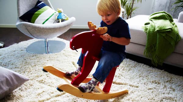A child riding a red IKEA EKORRE rocking-moose made from rubberwood from responsibly managed forests in Asia.