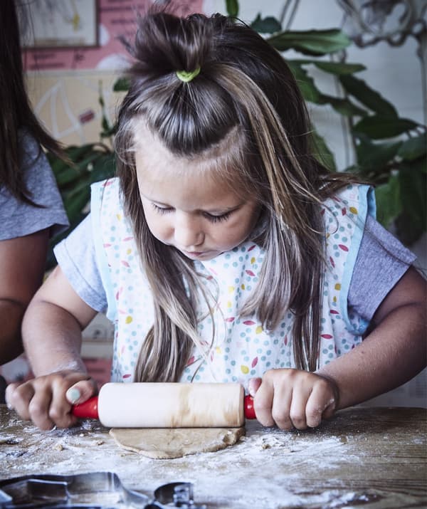 A child rolling dough with a rolling pin on a floured work surface.
