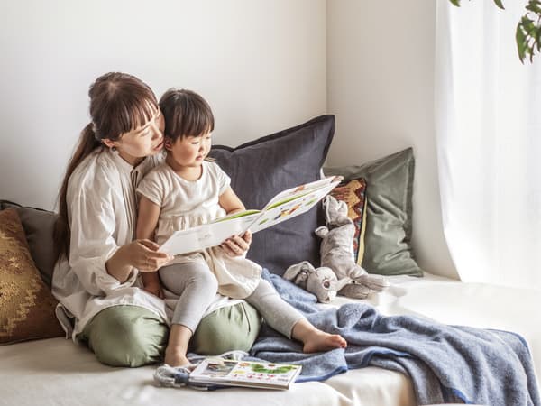 A child sitting on an adult's lap reading a picture book together.