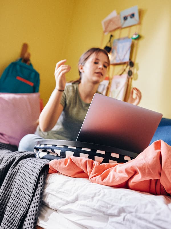 A child studies on her computer while sat on her bed, the laptop held steady by a BYLLAN laptop support.