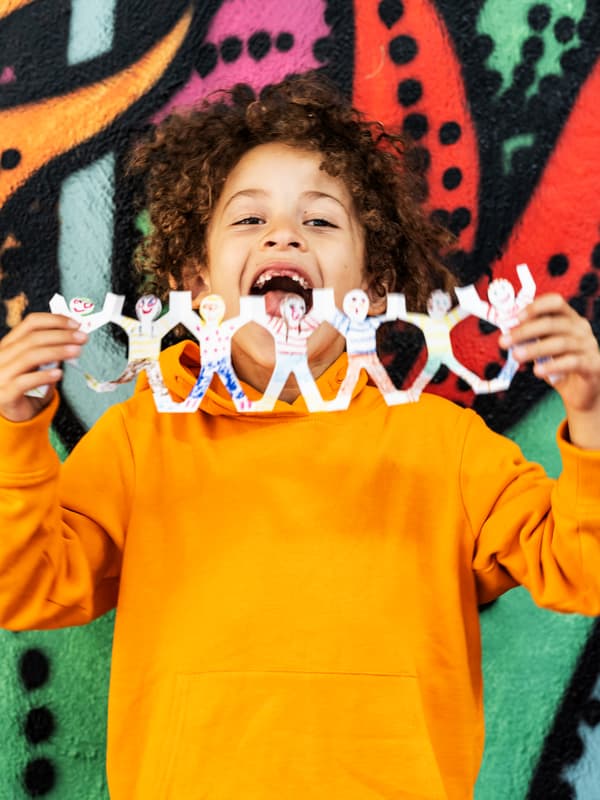 A child with an orange sweater holds a playful garland in front of a colourful wall.