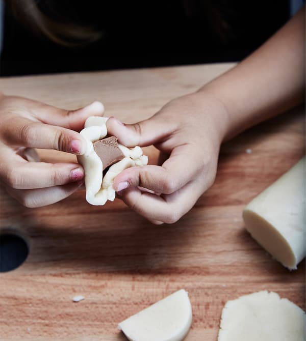 A child wraps marzipan around a piece of chocolate.