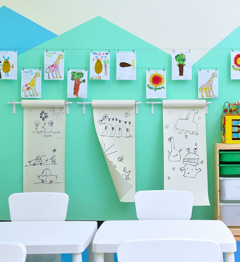 A childcare room where children's drawings are displayed and hung against a turquoise and white wall. 