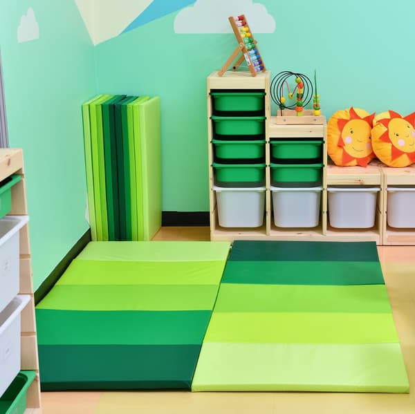 A children play area featuring playmats of different shades of green placed on the floor.