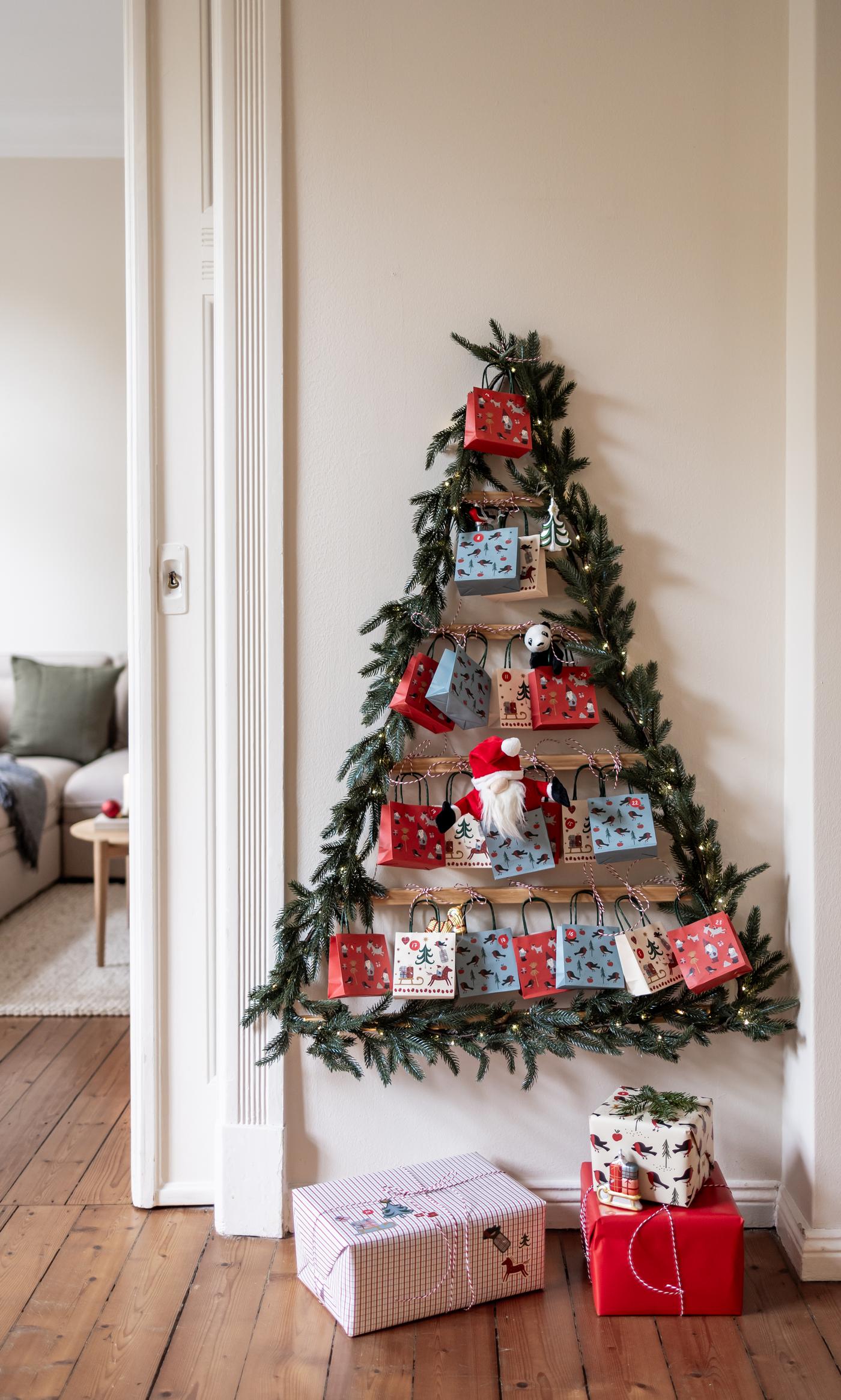 A children’s Advent calendar in the form of a Christmas tree hangs on a white wall with colourful gift packages.