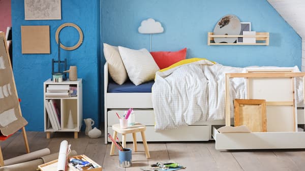A children's bedroom with artist tools, a VÄNKRETS quilt cover and pillowcase, and a white SMUSSLA bedside table/shelf unit.