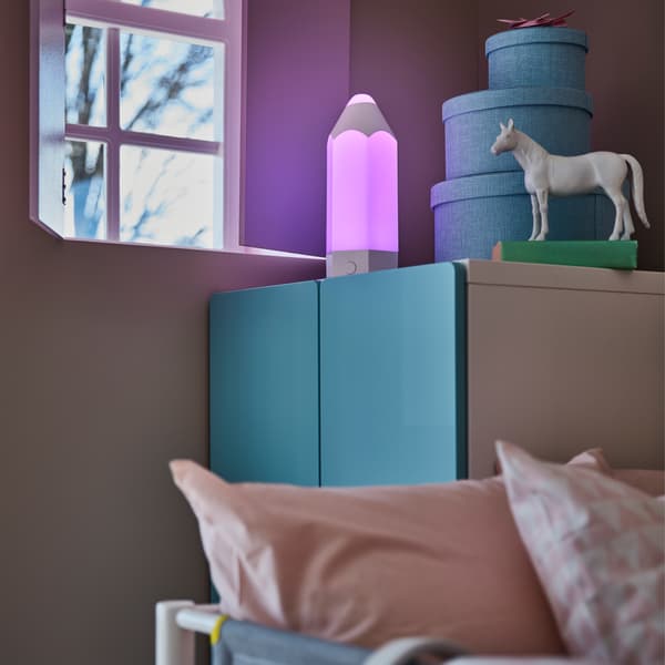 A children's room in an evening setting with a close-up of a blue wardrobe and PELARBOJ table lamp that gives a purple glow.