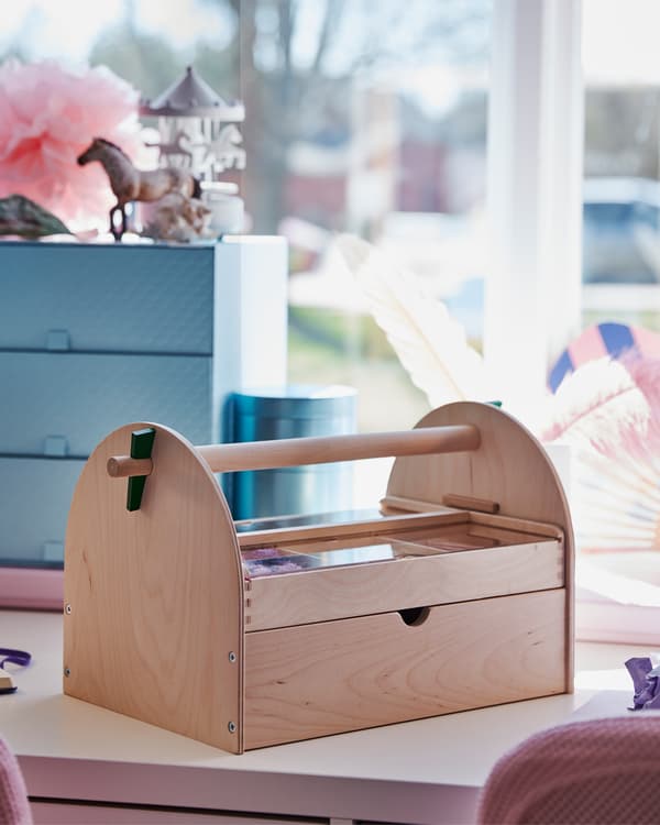 A children's room with a close up of a crafts storage that is standing on a white desk with a blue decoration box behind it.