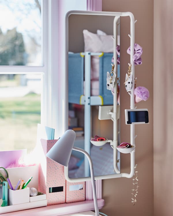 A children's room with a close-up of MÖJLIGHET white mirror that holds a phone, pink hair accessories and a necklace.
