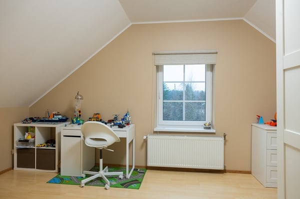 A children’s study area in an attic room featuring a desk, chair, shelving with toys, and a window providing natural light.