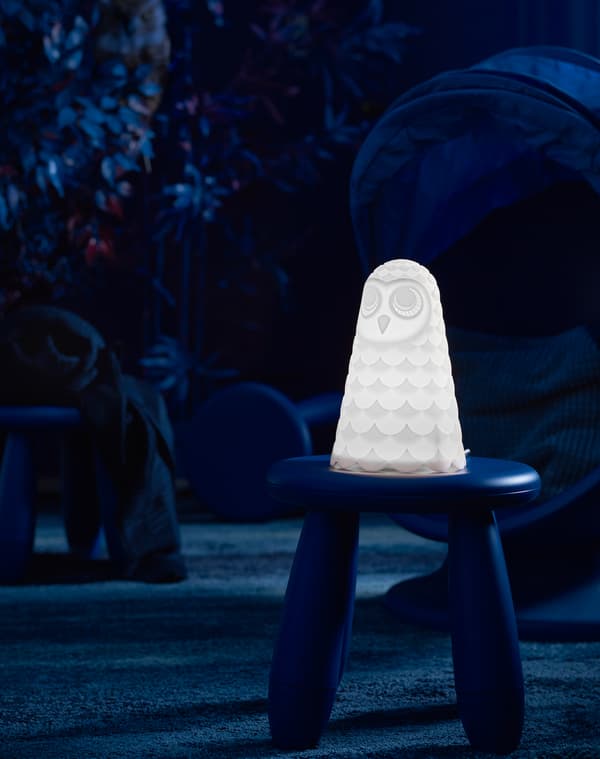 A children’s white owl IKEA SOLBO LED table lamp sitting on a plastic stool in a darkened kid’s play area.