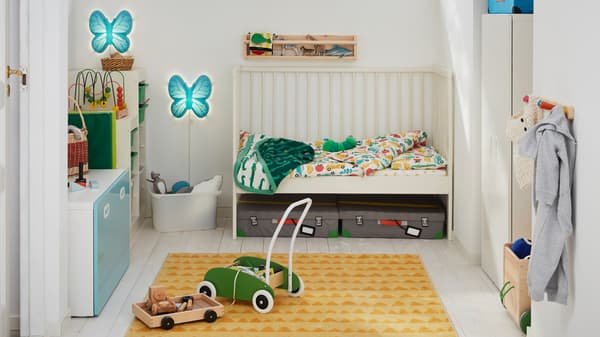 A child’s bedroom with a white GULLIVER cot with one side removed and a green MULA toddle truck on a RÖRANDE rug.