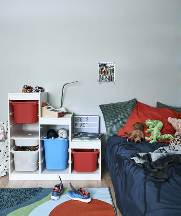 A child’s bedroom with colourful storage unit, rug and bed with cushions and toys.