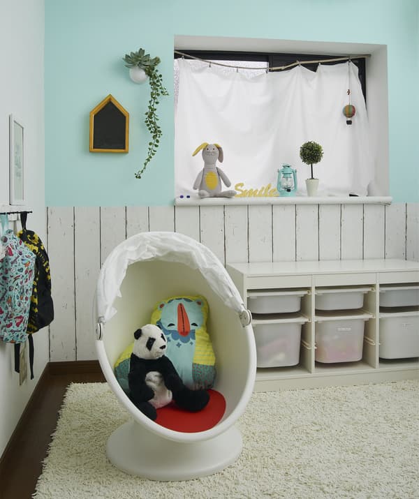 A child’s playroom with storage boxes and soft toys in a child’s armchair on a rug.