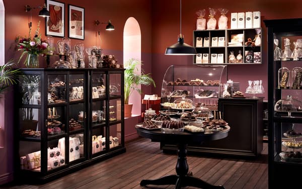A chocolaterie with IKEA MALSJÖ black stained cabinets with glass doors and brown walls, displaying various wrapped candy.