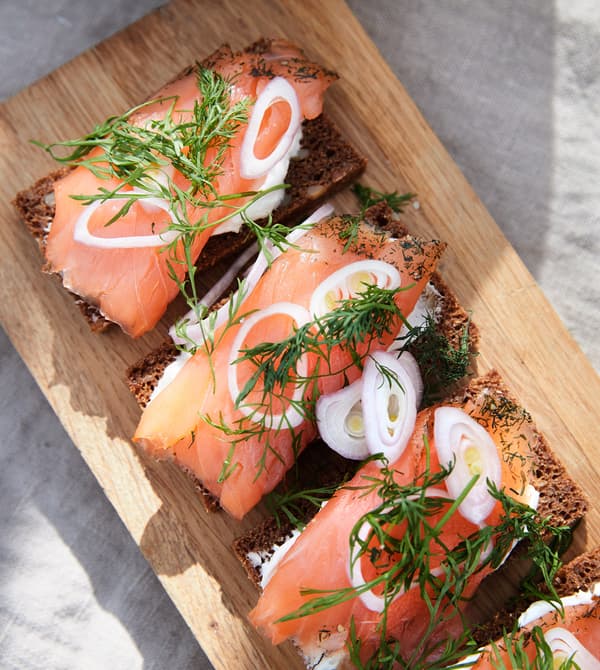 A chopping board with rye bread and smoked salmon with pickled vegetables and dill.