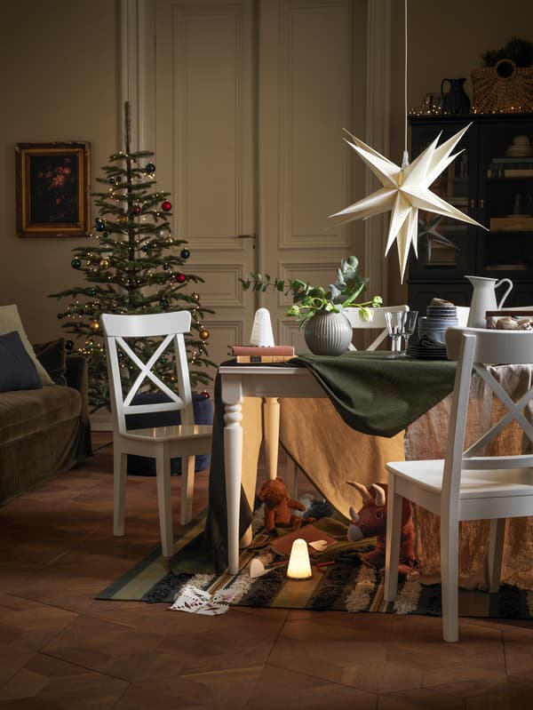 A Christmas tree and dining table stand in a festive living room, with a secret den full of toys shown under the table.