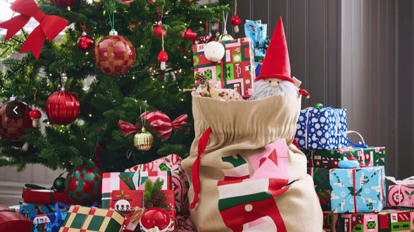 A christmas tree with many gifts and a bag overflowing with presents 