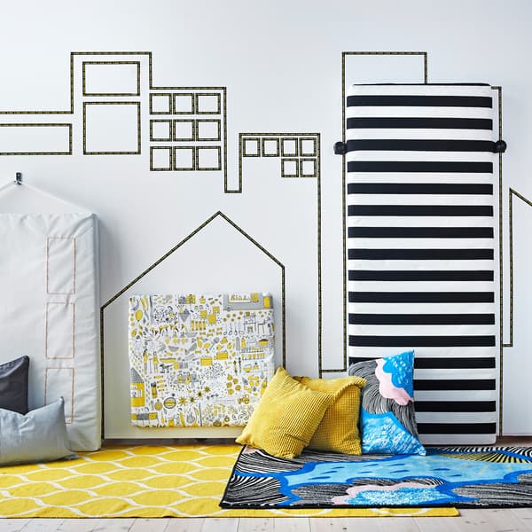 A city skyline is created on a bedroom wall using decorative tape and mattresses covered in textiles.