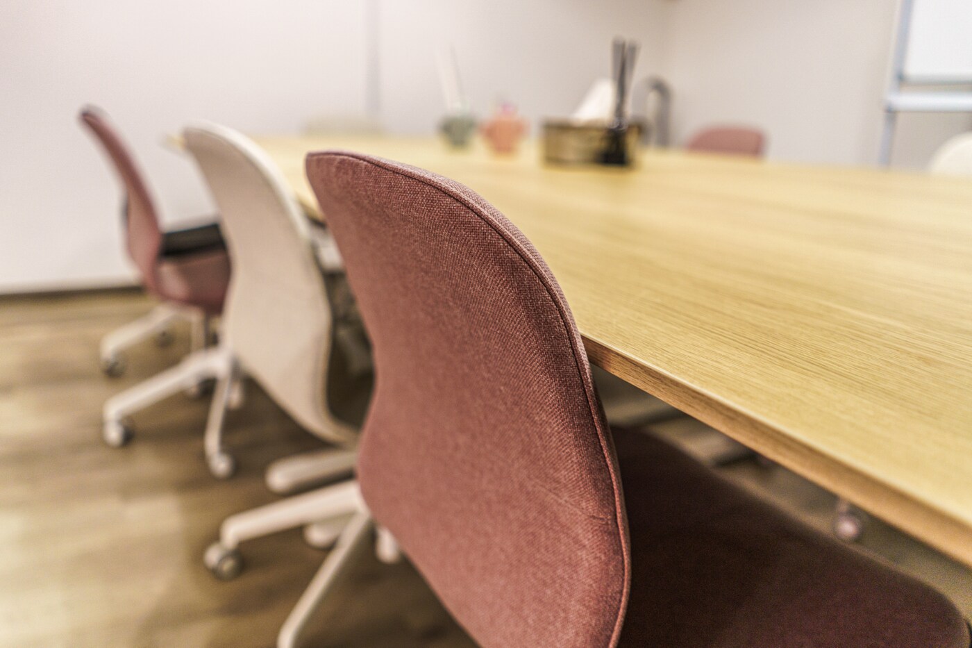 A classroom space featuring wooden desks and swivel chairs of various colours.
