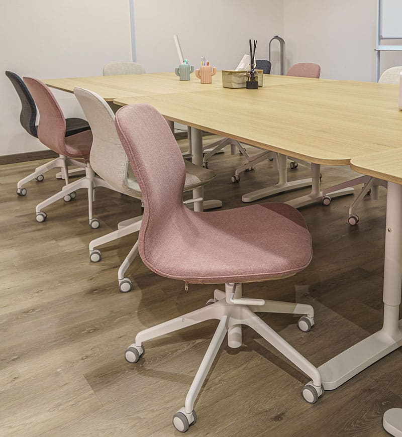 A classroom space featuring wooden desks and swivel chairs of various colours.