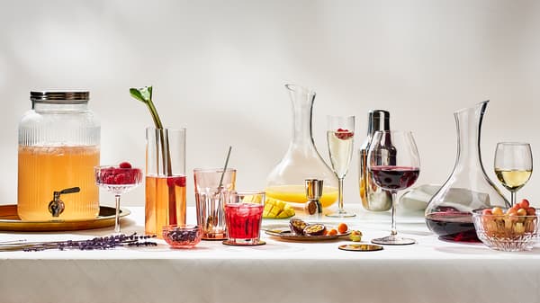 A clear glass carfe and different drinks in various wine glasses and drinking glasses on a table with a white tablecloth.