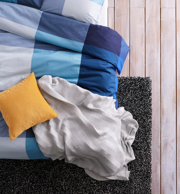 A close up image of a bed with blue, grey and yellow bedding and textiles.