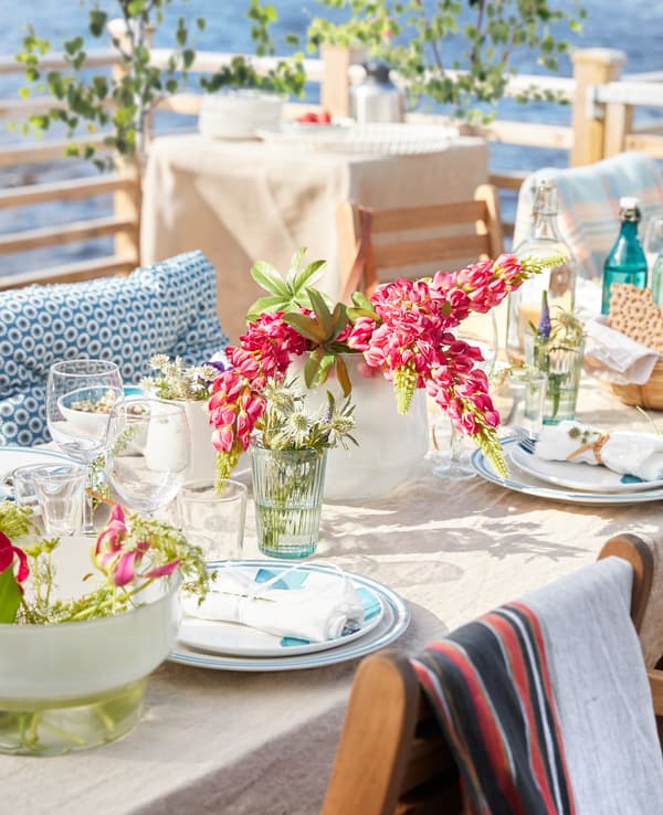 A close-up image of a dining table set for a meal, with a vase of flowers and table linens.