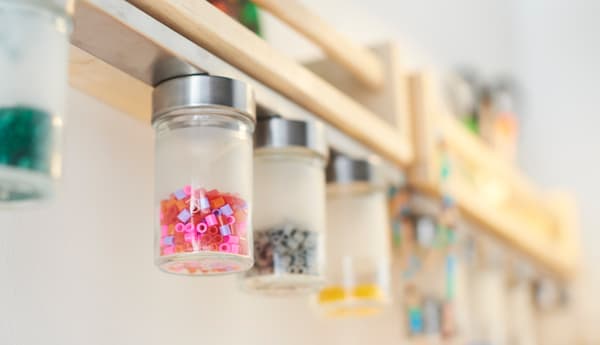  A close-up image of a magnetic knife rack holding jars of beads under a small wooden shelf.