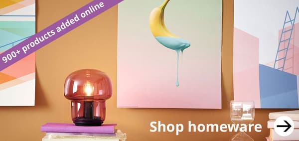 A close up image of a pastel coloured room with a purple glass lamp in the foreground and pastel coloured posters on a sand coloured wall.