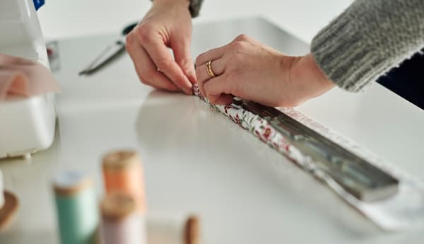 A close-up image of a woman gluing a floral textile to a magnetic knife wrap.