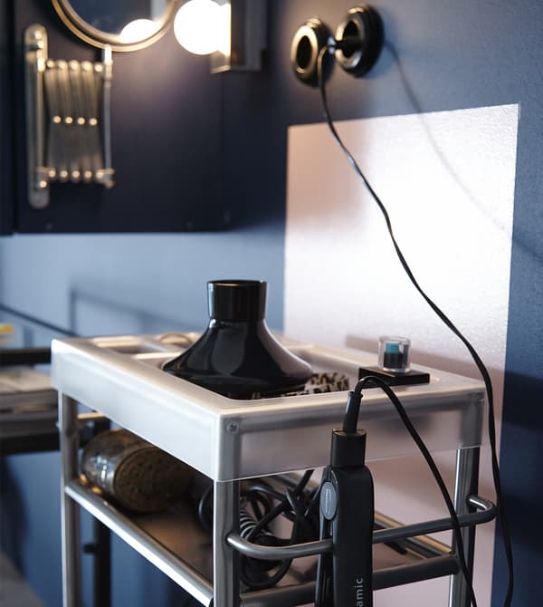 A close-up image of an IKEA GRUNDTAL cart stocked with blowdryers, curling irons, and other accessories.