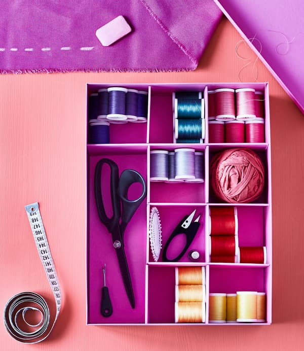 A close-up image of an IKEA TJENA box filled with different coloured spools of thread and sewing supplies.