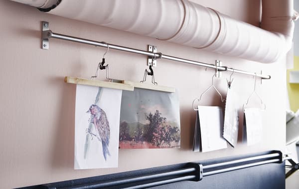A close-up image of artwork hung with hanger from a rail mounted between pipes.
