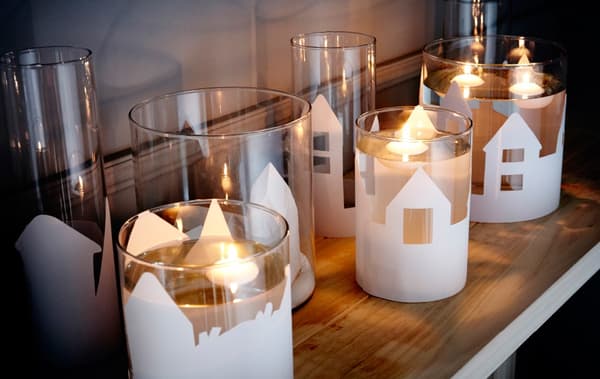 A close-up image of different sizes of IKEA CYLINDER vases, decorated with paper cutouts of landscapes, filled with water and a floating candle.