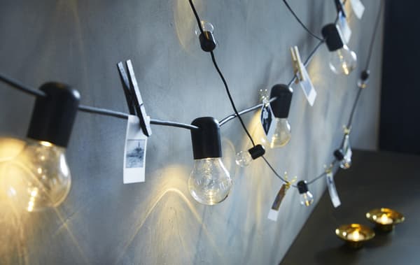 A close up image of lit string lights hanging on a wall with photos clipped to the wires for decoration.