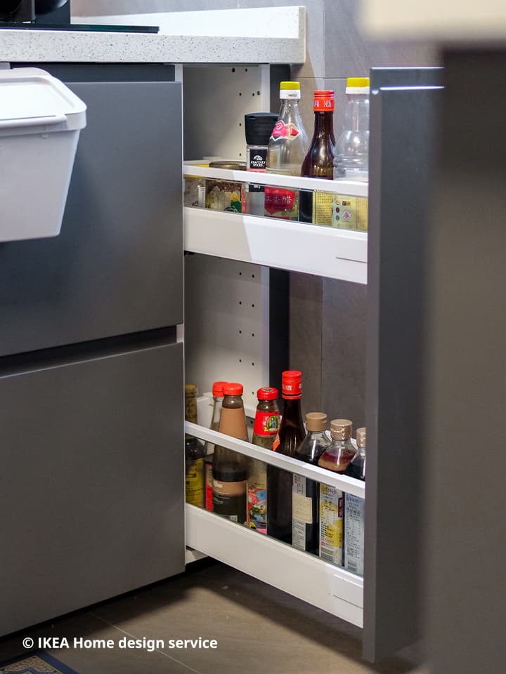 A close up look of a pull-out drawer in the base cabinet of IKEA METOD kitchen system, filled with different bottles of sauces and seasonings for cooking.