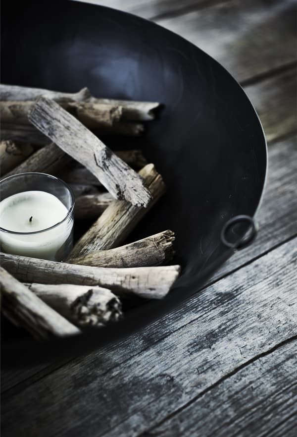 A close-up of a black bowl decorated with a white candle in a glass and wooden sticks.
