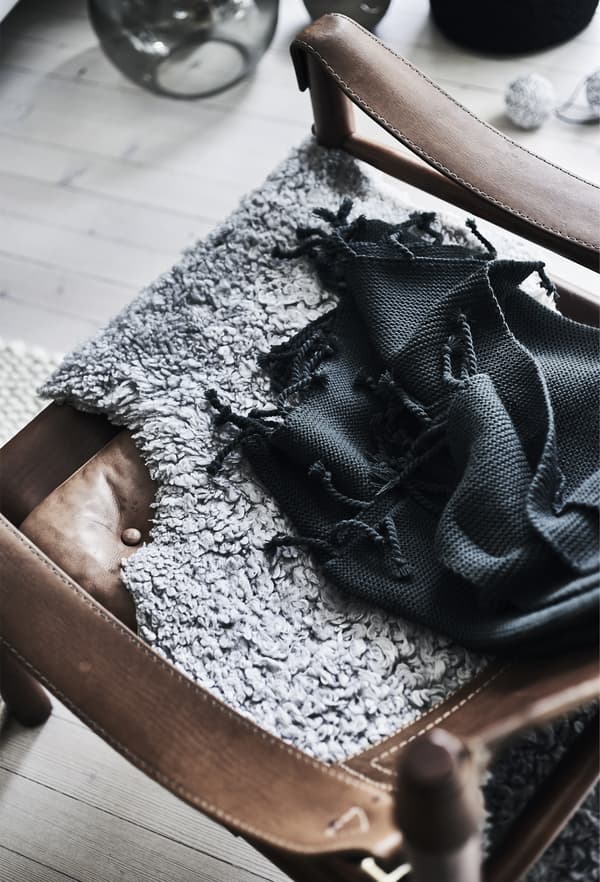 A close-up of a black throw and grey sheepskin draped over a brown leather armchair.