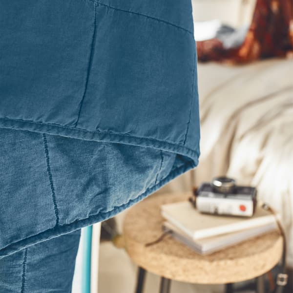 A close-up of a blue bedspread with neutral interior in the background.