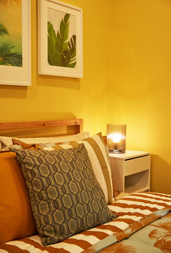 A close-up of a cushion on a bed in a yellow room. 