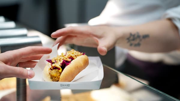 A close-up of a hand reaching for the IKEA veggie hot dog.