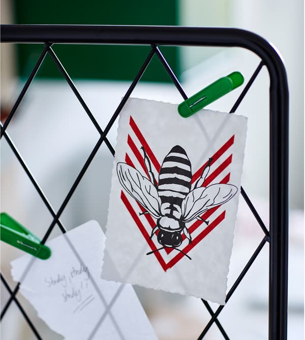 A close-up of a large black metal trellis with pictures and notes clipped to it.