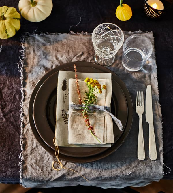 A close-up of a place setting with natural tones, dyed linens and small decorative pumpkins.