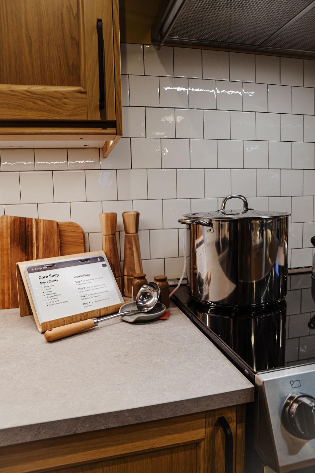 A close-up of a stainless steel pot sitting on a stove with kitchen accessories sitting on the counter.