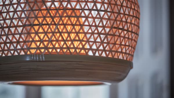A close-up of a switched on MISTERHULT pendant lamp handwoven in the light, natural material bamboo.