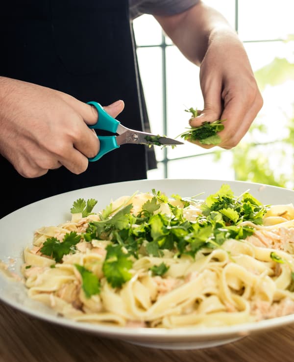 A close-up of a teenager cutting coriander onto pasta